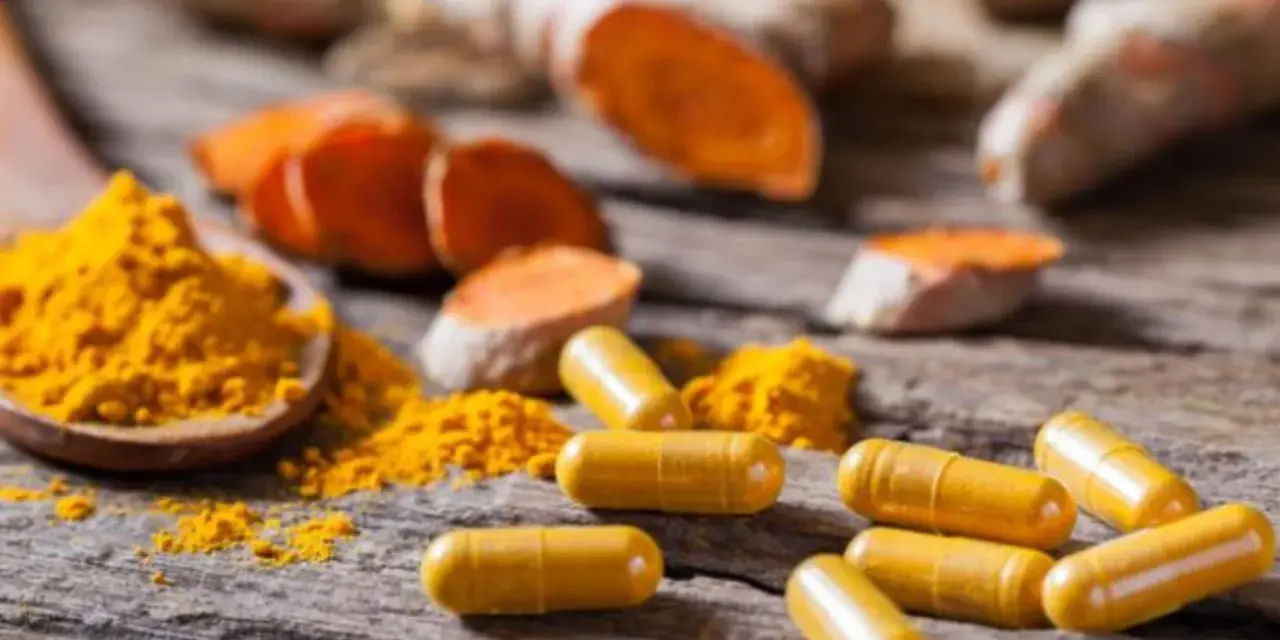Cápsulas amarillas y polvo de cúrcuma sobre madera rústica, destacando los beneficios de la curcuma en capsulas.