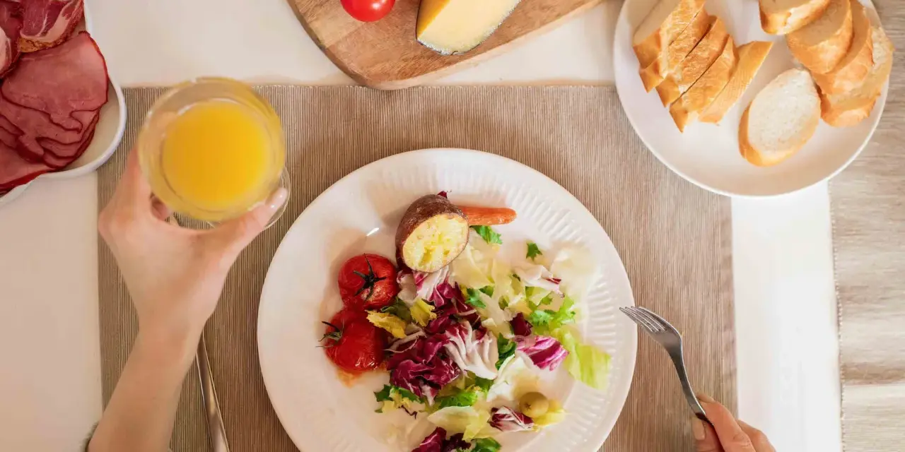 Persona disfrutando una ensalada, tomates, patata asada y un vaso de zumo, parte de su dieta intermitente 16/8.
