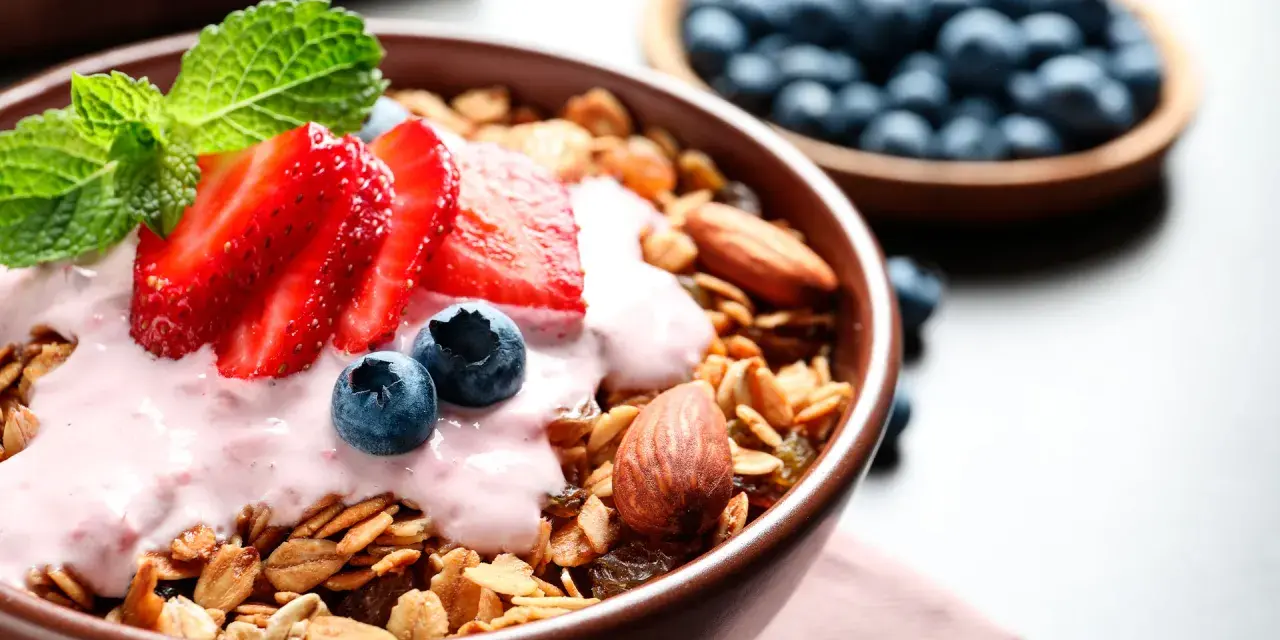Un tazón de qué es la granola, cubierto con yogur de fresa, fresas, arándanos y almendras.