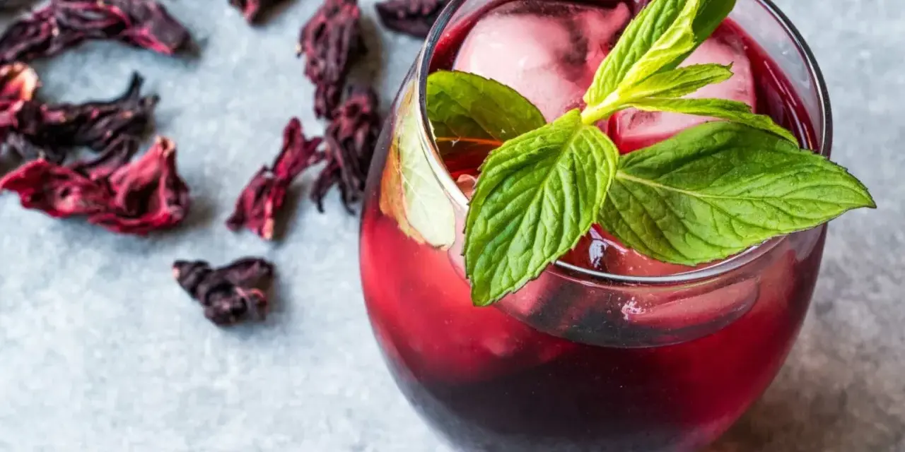 Refrescante vaso de agua de jamaica con hielo y menta, rodeado de flores secas de hibisco.