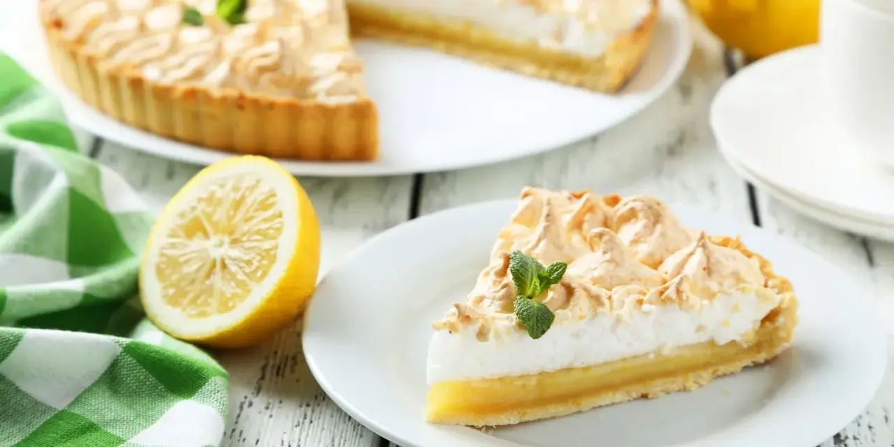 Un delicioso pastel de limón con merengue dorado, acompañado de limones frescos y una servilleta a cuadros verdes. Los ingredientes del lemon pie lucen perfectos.
