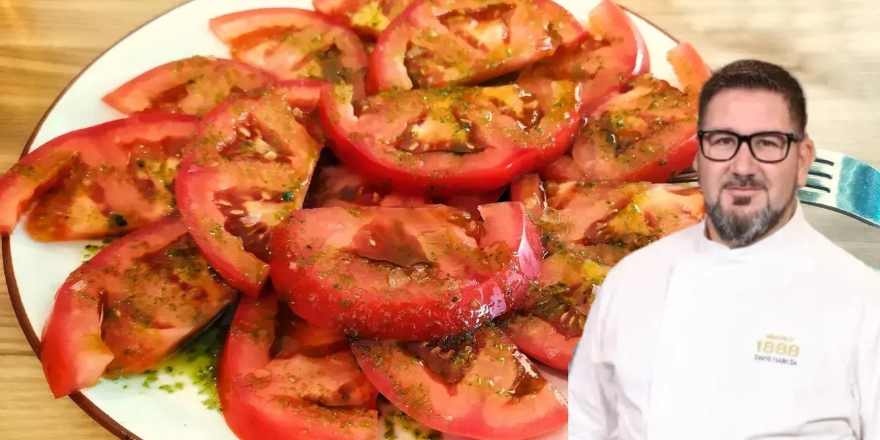 Un chef sonriente presenta un plato de tomate aliñado, fresco y jugoso, con un aderezo verde y aceite.
