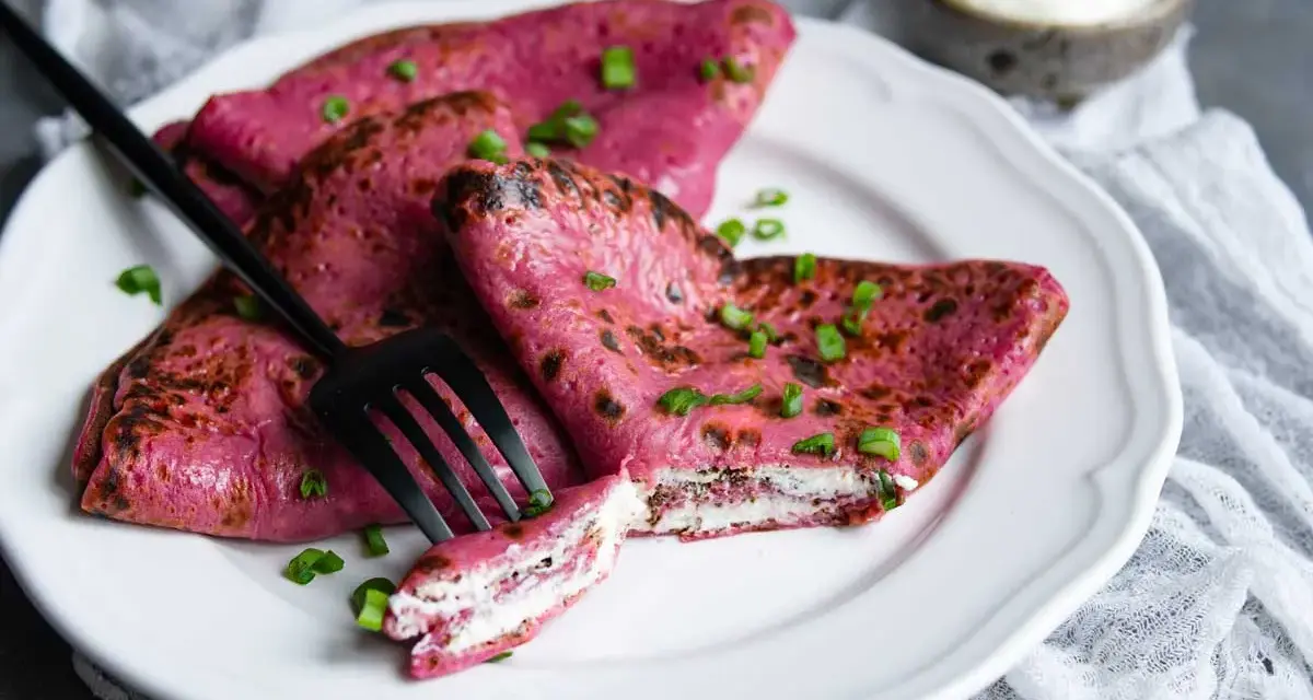 Crepes rosados ​​rellenos de queso crema, perfectos para recetas con remolacha cruda. Decorados con cebollín y acompañados de una porción de crema agria.