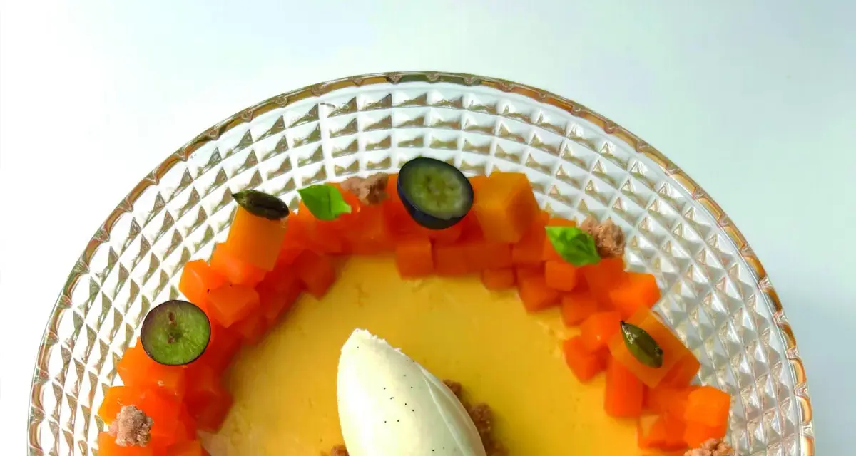 Delicioso flan de mango con helado de vainilla, trozos de mango fresco, arándanos y hojas de menta en un plato de cristal.