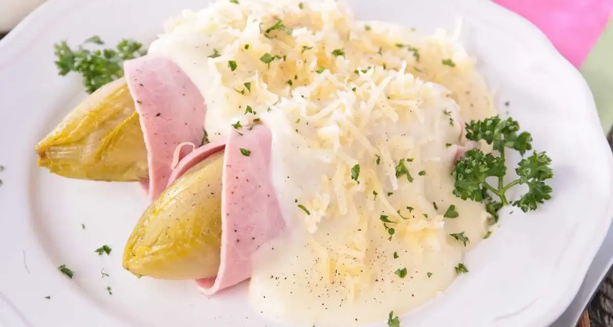 Endivias al horno envueltas en jamón, cubiertas con una cremosa salsa bechamel y queso rallado, adornadas con perejil fresco.
