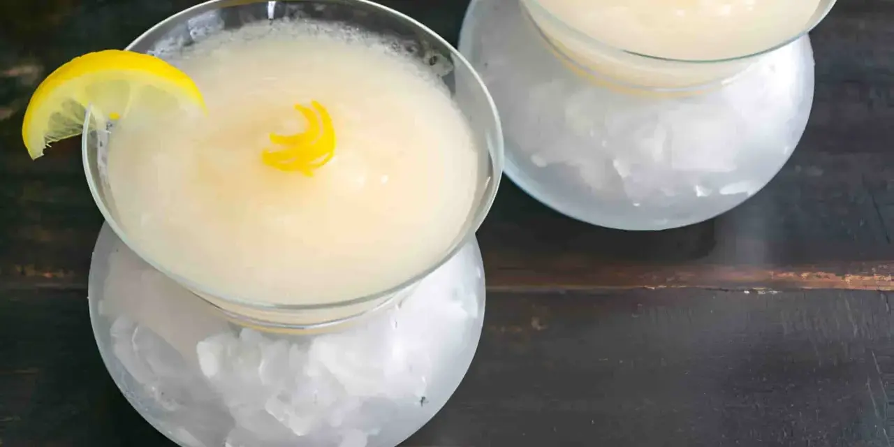 Dos copas de sorbete de limón, una con rodaja de limón y rizo de piel, servidas sobre hielo picado.