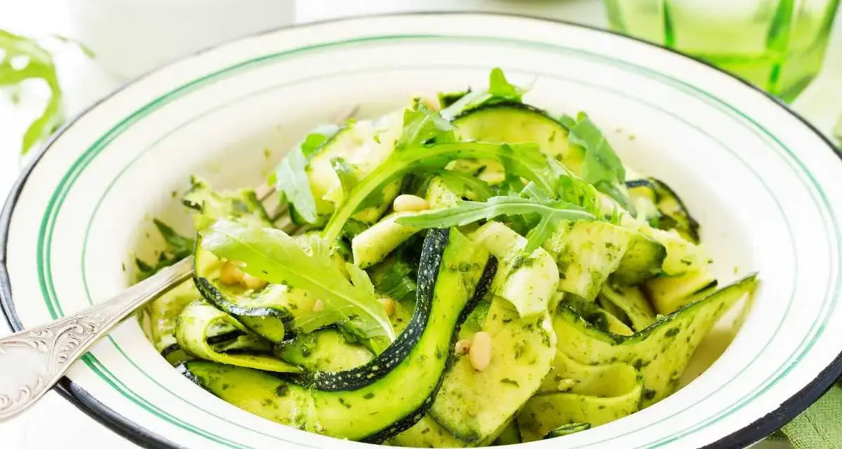 Deliciosa ensalada de calabacín en espiral con pesto y rúcula, adornada con piñones. Un plato fresco y vibrante.