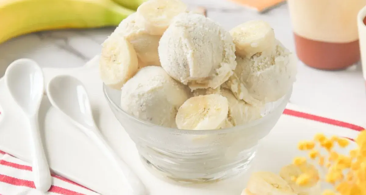 Delicioso helado de platano casero, cremoso y refrescante, servido en un cuenco de cristal con rodajas de plátano fresco.