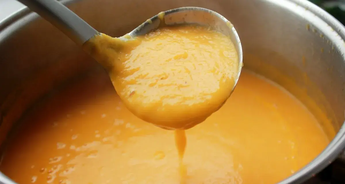 Cucharón sirviendo una deliciosa crema de zanahoria y puerro recién hecha de una olla.