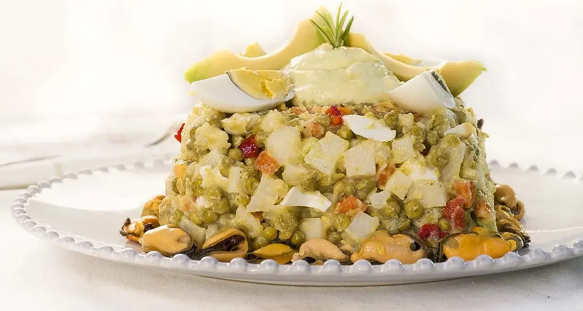 Deliciosa ensaladilla de aguacate con huevo duro, guisantes y mejillones, coronada con una crema suave y rodajas de aguacate fresco.