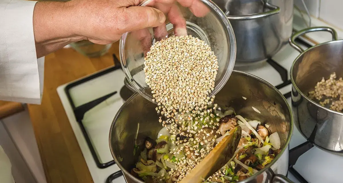 Mano añade trigo sarraceno a una olla con verduras y champiñones.