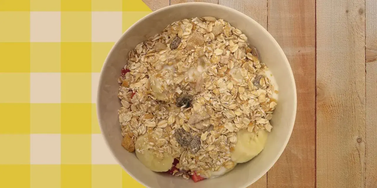 Un tazón de porridge de avena con plátano, fresas y pasas, servido sobre un mantel a cuadros amarillos y blancos.