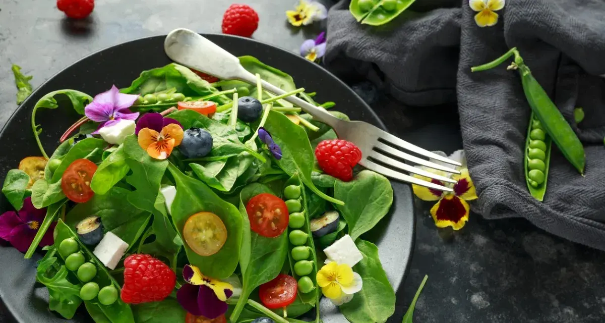 Ensalada vibrante con frambuesas, arándanos, guisantes y flores comestibles, celebrando las frutas de primavera.