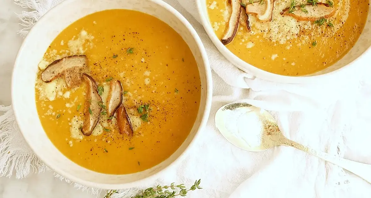 Dos tazones de cremosa sopa de calabaza, adornados con champiñones y queso rallado, listos para ser disfrutados.