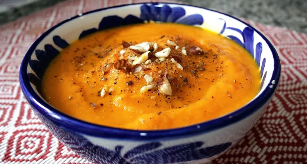 Crema de zanahoria y jengibre, servida en un cuenco azul y blanco, adornada con nueces y pimienta.