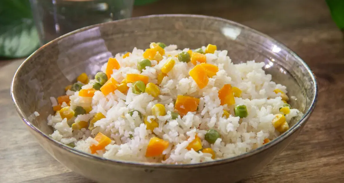 Un tazón de arroz blanco con trozos de zanahoria, guisantes y maíz. Un plato sencillo y colorido de arroz con verduras.