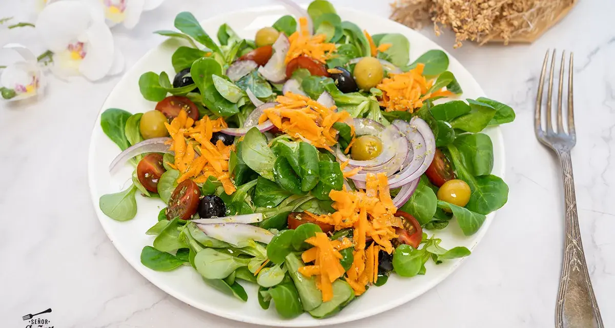 Deliciosa ensalada mediterránea con lechuga, tomate, aceitunas, cebolla morada y zanahoria rallada.