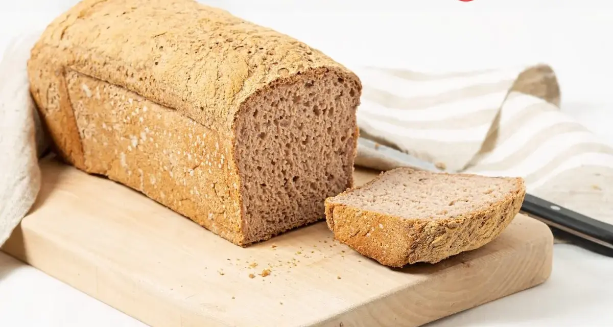 Pan sin gluten recién horneado, con una rebanada lista para disfrutar. Su textura porosa y corteza dorada invitan a probarlo.