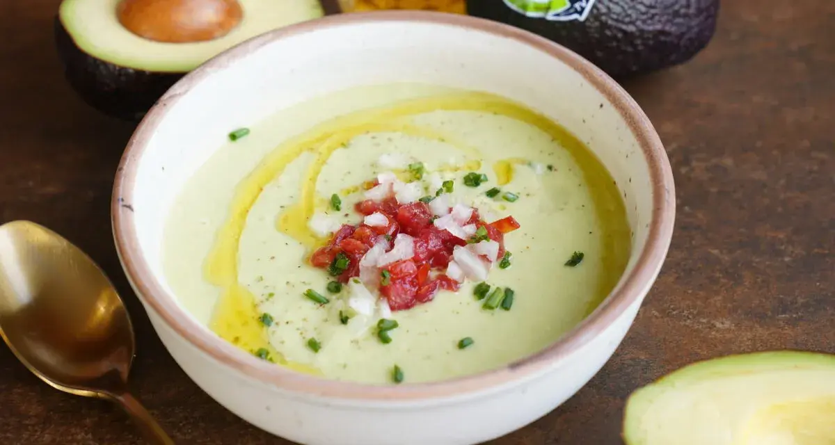 Un cremoso gazpacho de aguacate, adornado con tomate picado, cebolla y cebollino, con un chorrito de aceite de oliva.
