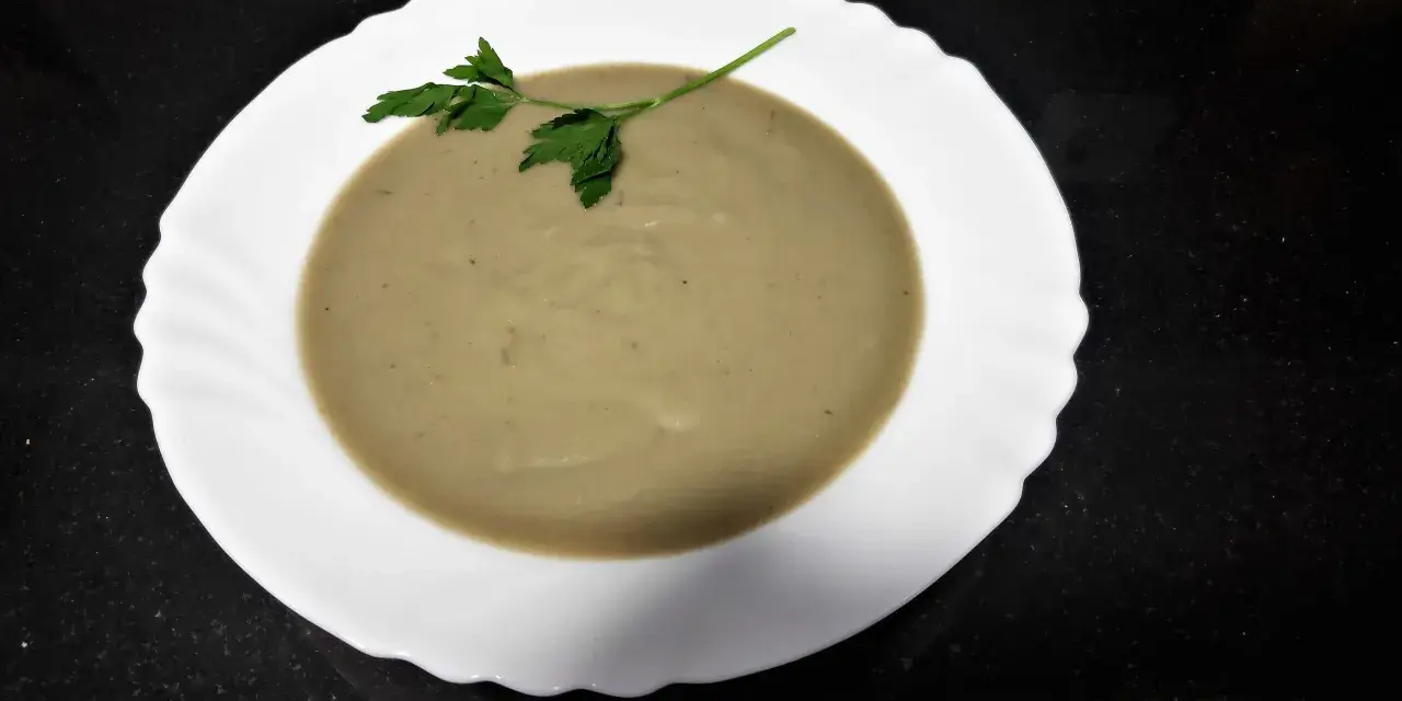 Crema de berenjena suave y sedosa, decorada con una ramita de perejil fresco, lista para disfrutar.