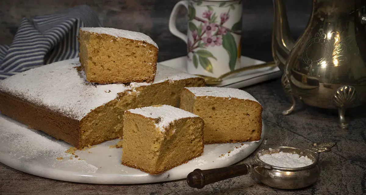 Un delicioso bizcocho de mango, espolvoreado con azúcar glas, listo para disfrutar con una taza de té.
