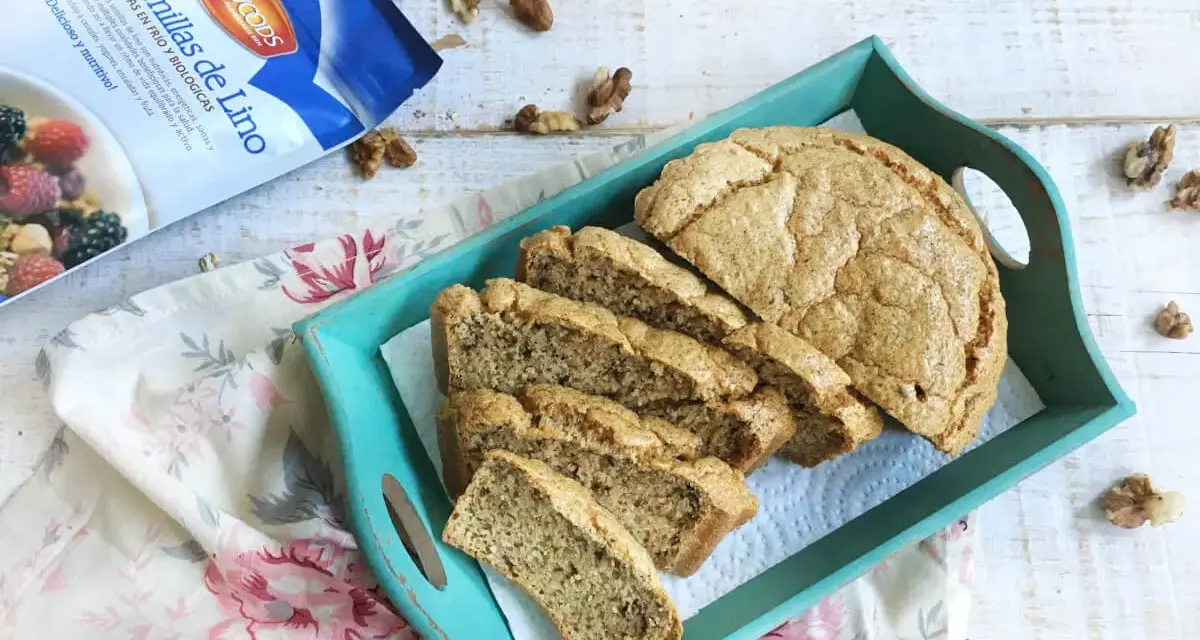 Rebanadas de pan de lino en una bandeja turquesa, junto a un paquete de semillas de lino y nueces.