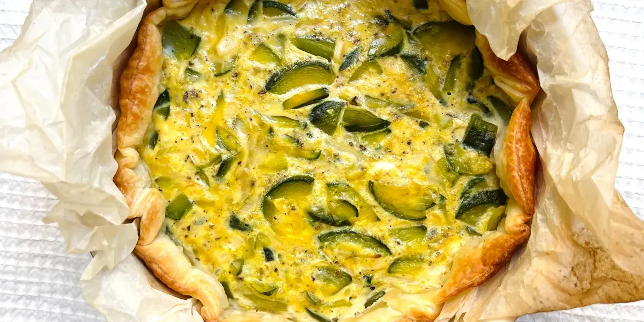 Quiche de calabacín recién horneada, con masa dorada y relleno cremoso salpicado de trozos verdes.