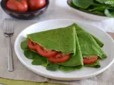 Deliciosos crepes de espinacas rellenos de rodajas de tomate fresco y hojas de espinaca, servidos en un plato blanco.