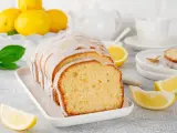 Un delicioso budín de limón glaseado, con rodajas de limón fresco y una taza de té al fondo.