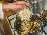 Mano añade trigo sarraceno a una olla con verduras y champiñones.