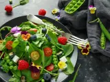 Ensalada vibrante con frambuesas, arándanos, guisantes y flores comestibles, celebrando las frutas de primavera.
