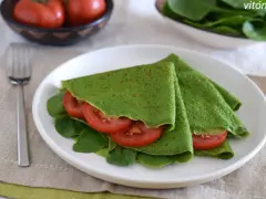 Deliciosos crepes de espinacas rellenos de rodajas de tomate fresco y hojas de espinaca, servidos en un plato blanco.