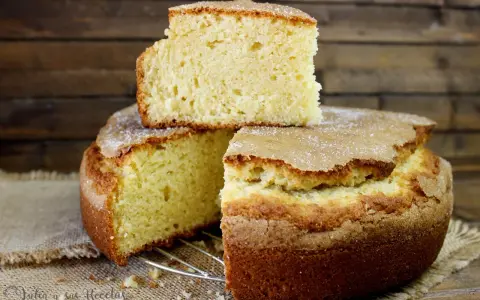 El bizcocho de limón de la abuela, esponjoso y dorado, con una capa de azúcar espolvoreada. Un trozo descansa sobre el pastel principal.