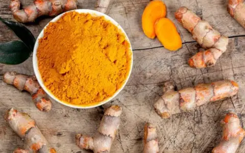 Raíces de cúrcuma y polvo dorado en un cuenco. Descubre qué es la cúrcuma y para qué sirve, un tesoro natural.