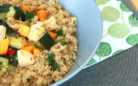 Un tazón de quinoa con pollo y verduras salteadas, como calabacín y zanahoria.
