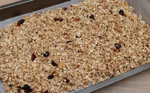 Granola de avena casera lista para hornear, con frutos secos y pasas, extendida en una bandeja.