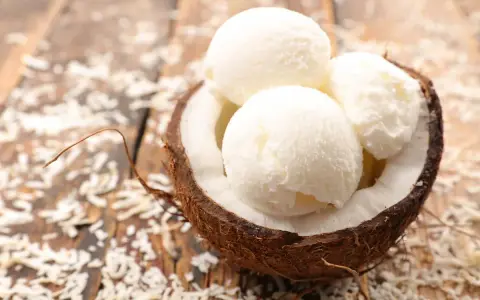 Delicioso helado con leche de coco servido en una cáscara de coco, espolvoreado con coco rallado sobre una mesa de madera.