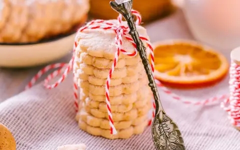 Deliciosas galletas de naranja, apiladas y atadas con hilo rojo y blanco. Una rodaja de naranja y una cuchara antigua completan la escena.