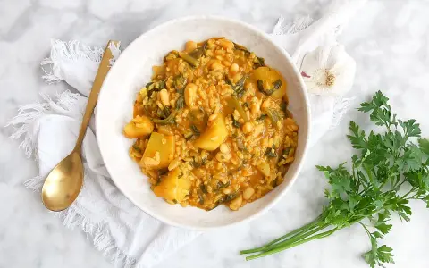 Un tazón de arroz con acelgas, patatas y alubias blancas, servido con una cuchara dorada y perejil fresco.