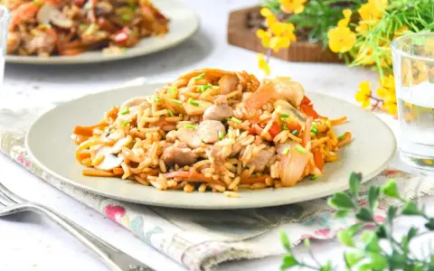 Un delicioso wok de verduras y arroz con trozos de pollo y champiñones, adornado con cebollino fresco.