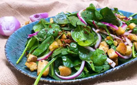 Ensalada de espinacas frescas con crutones, cebolla morada y aderezo en un plato azul.