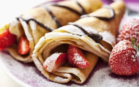 Deliciosos crepes sin huevo rellenos de fresas y bañados en chocolate, espolvoreados con azúcar glas.