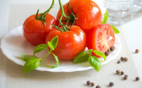 Tomates frescos con gotas de agua, albahaca y granos de pimienta, ingredientes naturales para productos antiinflamatorios.