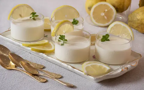 Delicioso postre de lemon curd receta original, servido en vasos con rodajas de limón y menta.