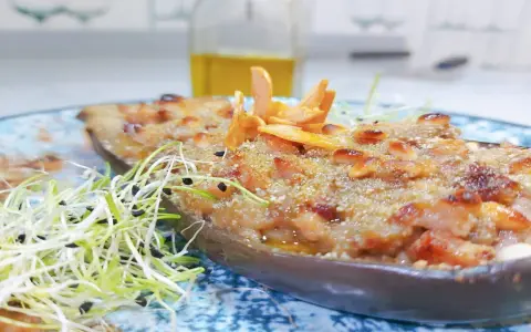Deliciosa berenjena rellena gratinada, adornada con piñones y brotes frescos, lista para ser disfrutada.