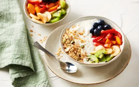 Un tazón de yogur cremoso con granola crujiente, arándanos, fresas, plátano, kiwi y melocotón.