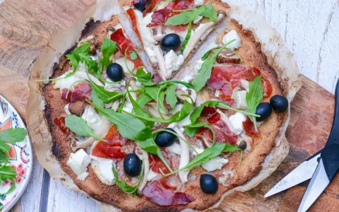 Pizza de quinoa con jamón serrano, aceitunas negras, champiñones y rúcula fresca. Una delicia saludable.