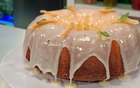 Delicioso budín de naranja con glaseado blanco y decorado con cáscaras de naranja confitada y hojas de menta.