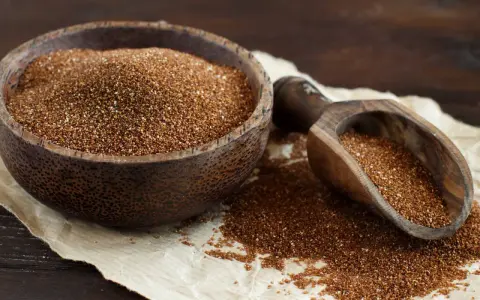 Un cuenco de madera lleno de teff cereal y una pala de madera con más granos.