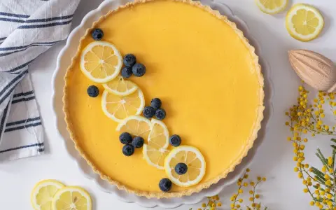 Tarta de limón al horno, decorada con rodajas de limón y arándanos. Un postre refrescante y vibrante.